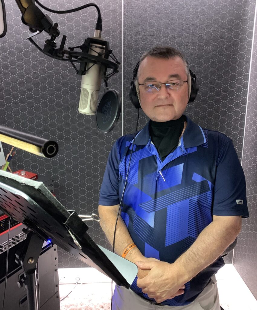 Wal Bak, a laryngectomee, standing next to microphone in a recording studio.